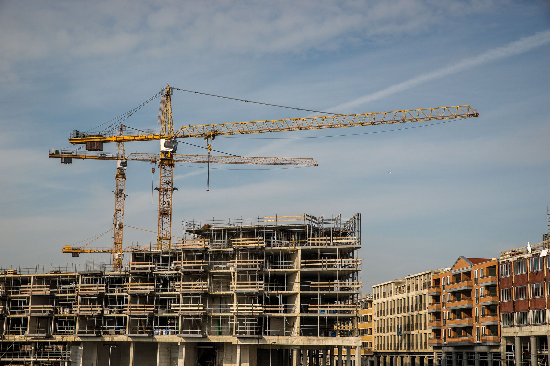 Yellow tower cranes above a concrete building under construction.